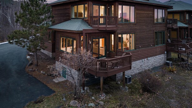 Eine zweistöckige Blockhütte mit einem Balkon, großen Fenstern und einem Schornstein.