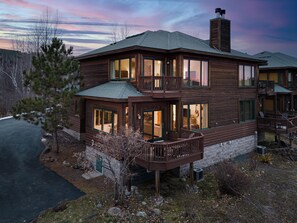 A two-story log cabin with a balcony, large windows, and a chimney.