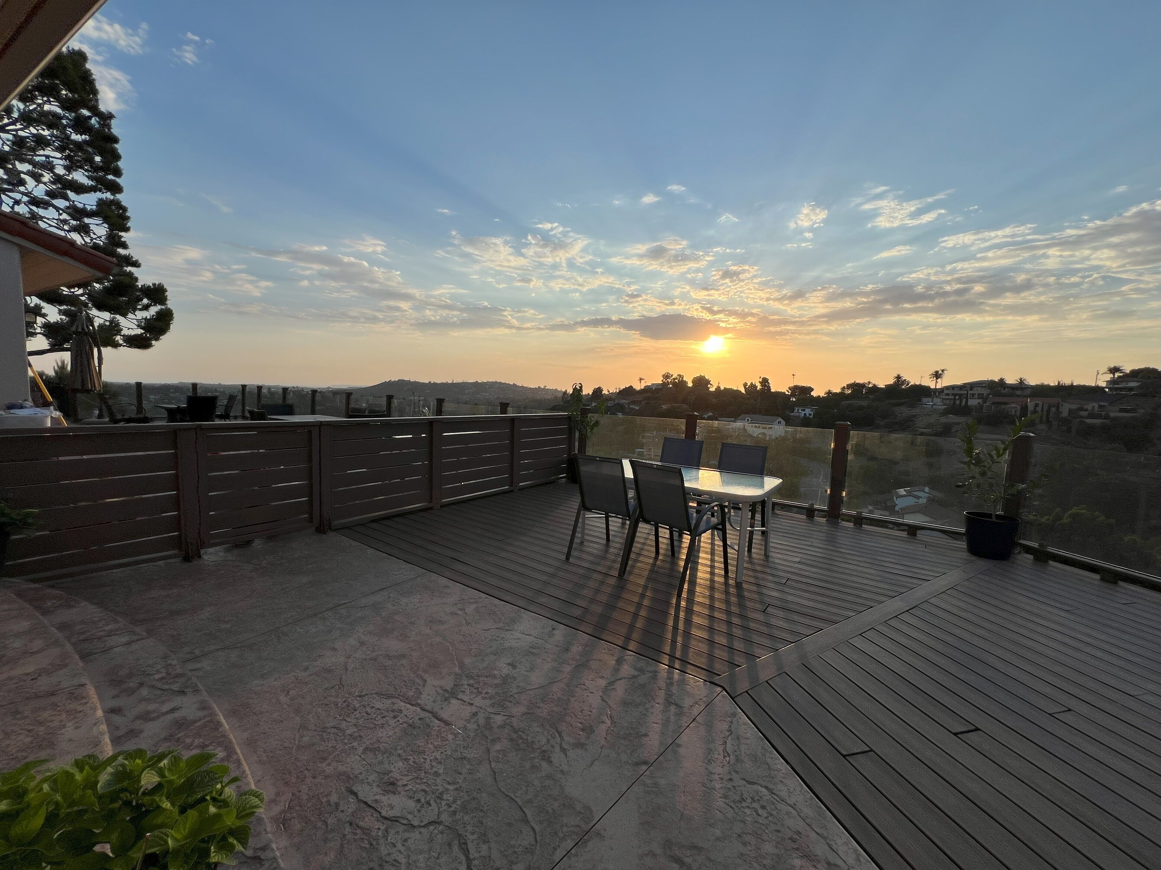 Una terraza de madera con una mesa y sillas, con vistas a un paisaje urbano al atardecer.