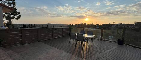 A wooden deck with a table and chairs, overlooking a cityscape during sunset.