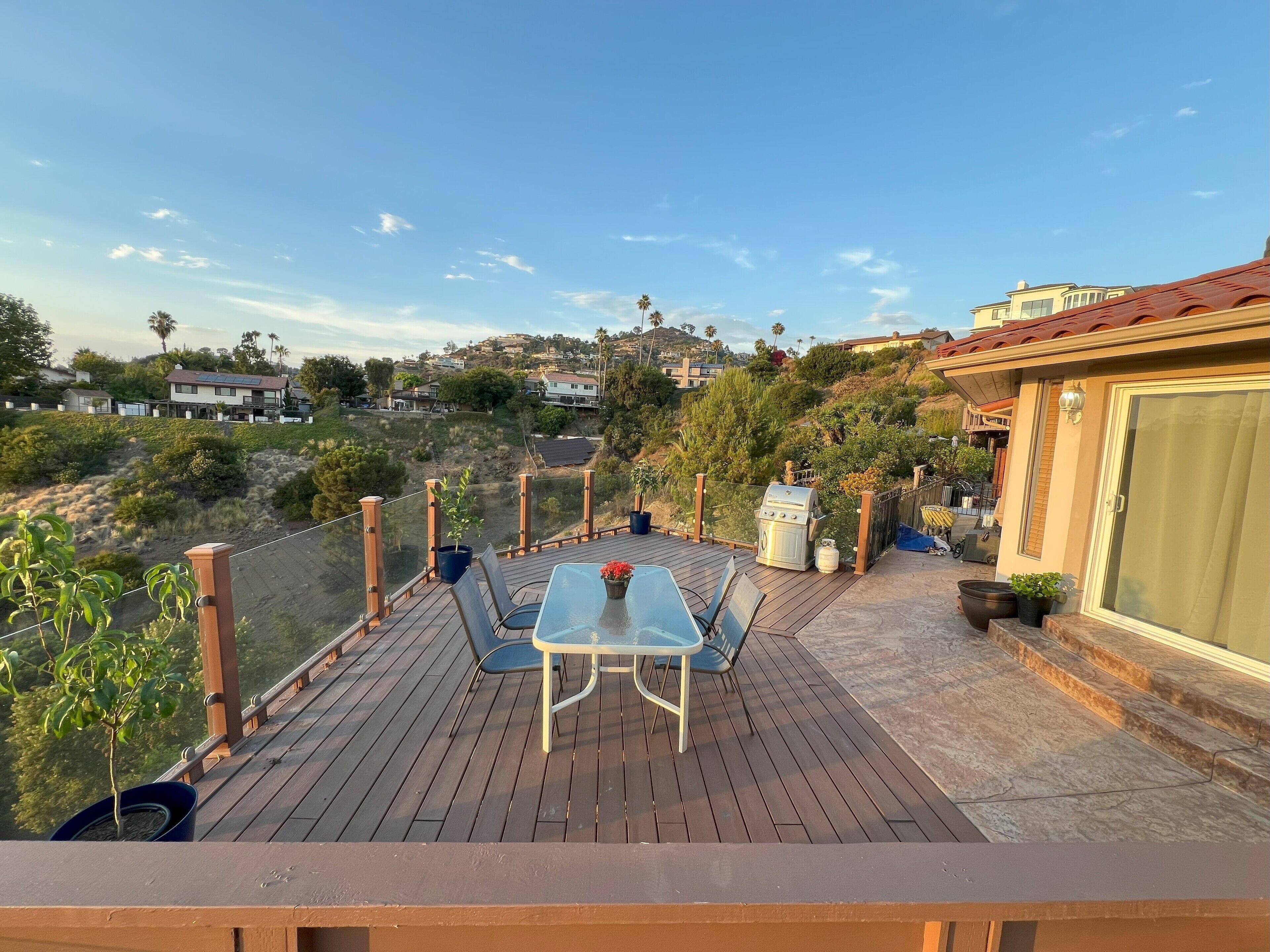 A wooden deck with a table and chairs, overlooking a hillside with houses and greenery.