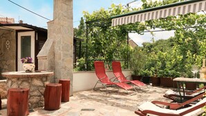 Une terrasse avec des fauteuils de jardin rouges, une cheminée en pierre et des plantes en pot.