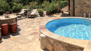 Une piscine bordée de pierres, entourée d’un patio aménagé avec des chaises longues et des plantes en pot.