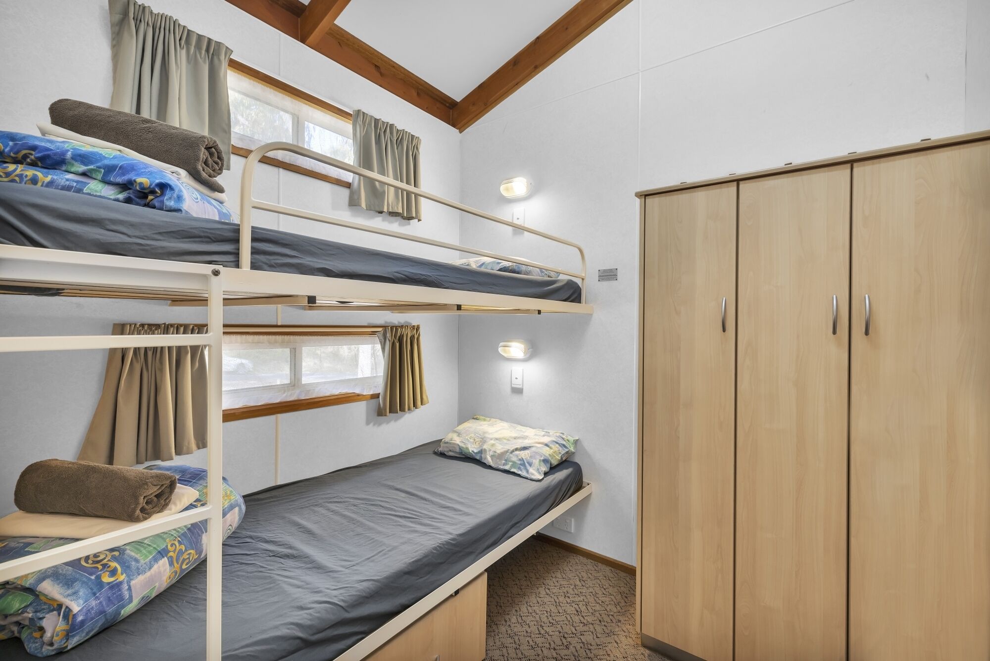 Dormitorio con literas, armario y dos ventanas.