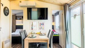 Een gezellige, compacte ruimte met een eethoek, een aan de muur bevestigde televisie en een bed op de achtergrond.