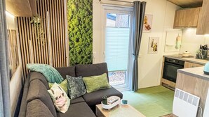 Een knus woongedeelte met een bank, een klein tafeltje, een keuken met oven en een groene wand.