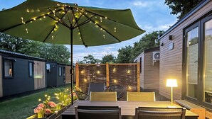 Een terras buiten met een houten tafel en stoelen, een grote parasol en lichtslingers.