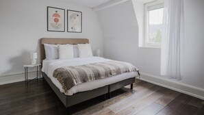 Quarto moderno com cama, mesas de cabeceira, janela com cortinas e obras de arte na parede.