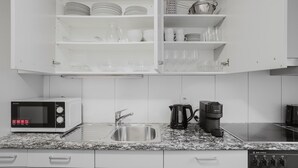 Uma cozinha moderna com armários brancos, uma pia de aço inoxidável, micro-ondas, cafeteira e lava-louça.