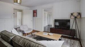 Uma sala de estar moderna com sofá, poltrona, mesa de centro, televisão e abajur.
