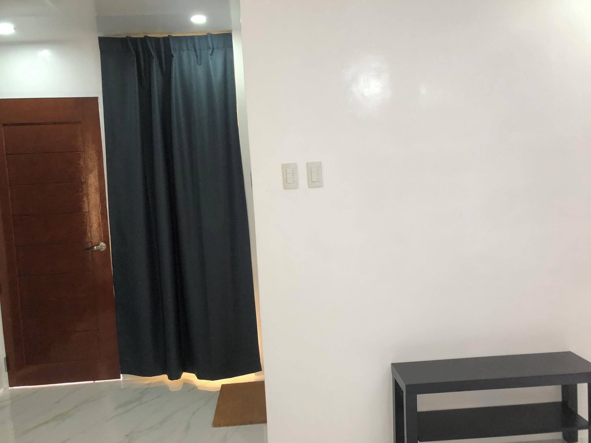 Una habitación con una puerta de madera, una cortina oscura, una pared blanca y una pequeña mesa negra.