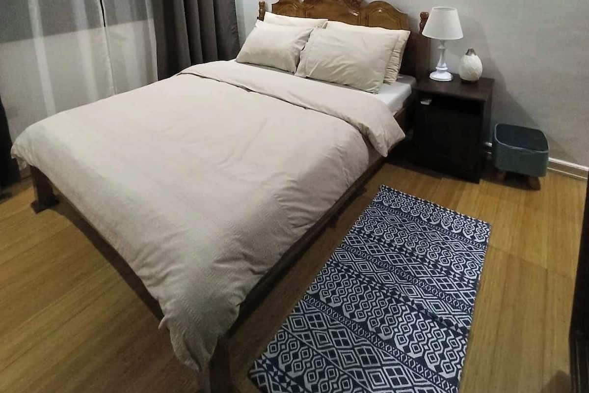 A neatly arranged bedroom with a bed, bedside table, lamp, and air conditioning unit.