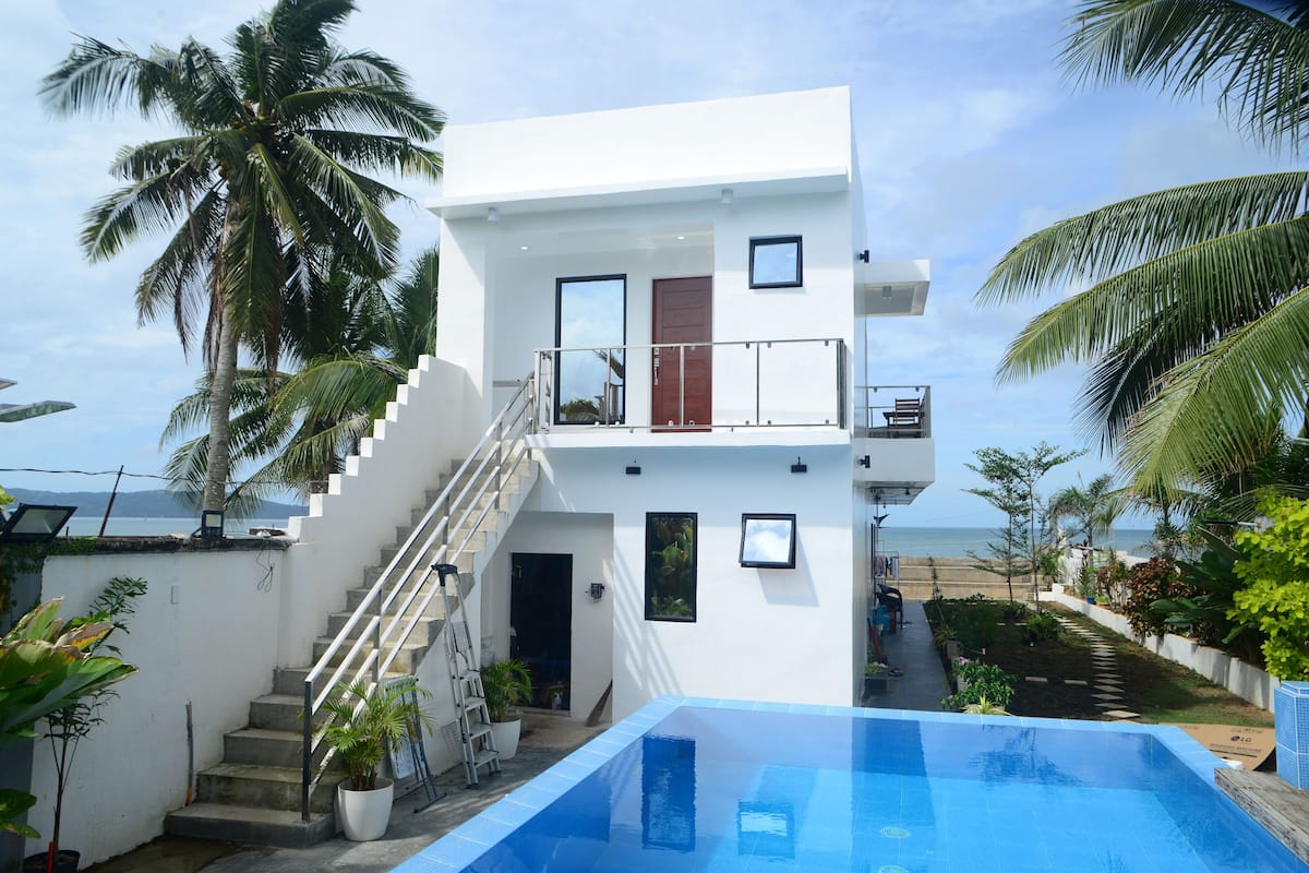 A modern two-story house with a swimming pool, a staircase, and a view of the beach.