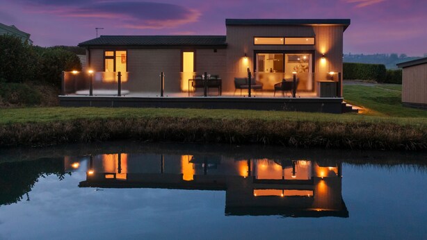 A modern house with a glass facade, a dining area, and a kitchen visible through the windows. - The Duck Pond - Countryside Hot Tub (Narberth)