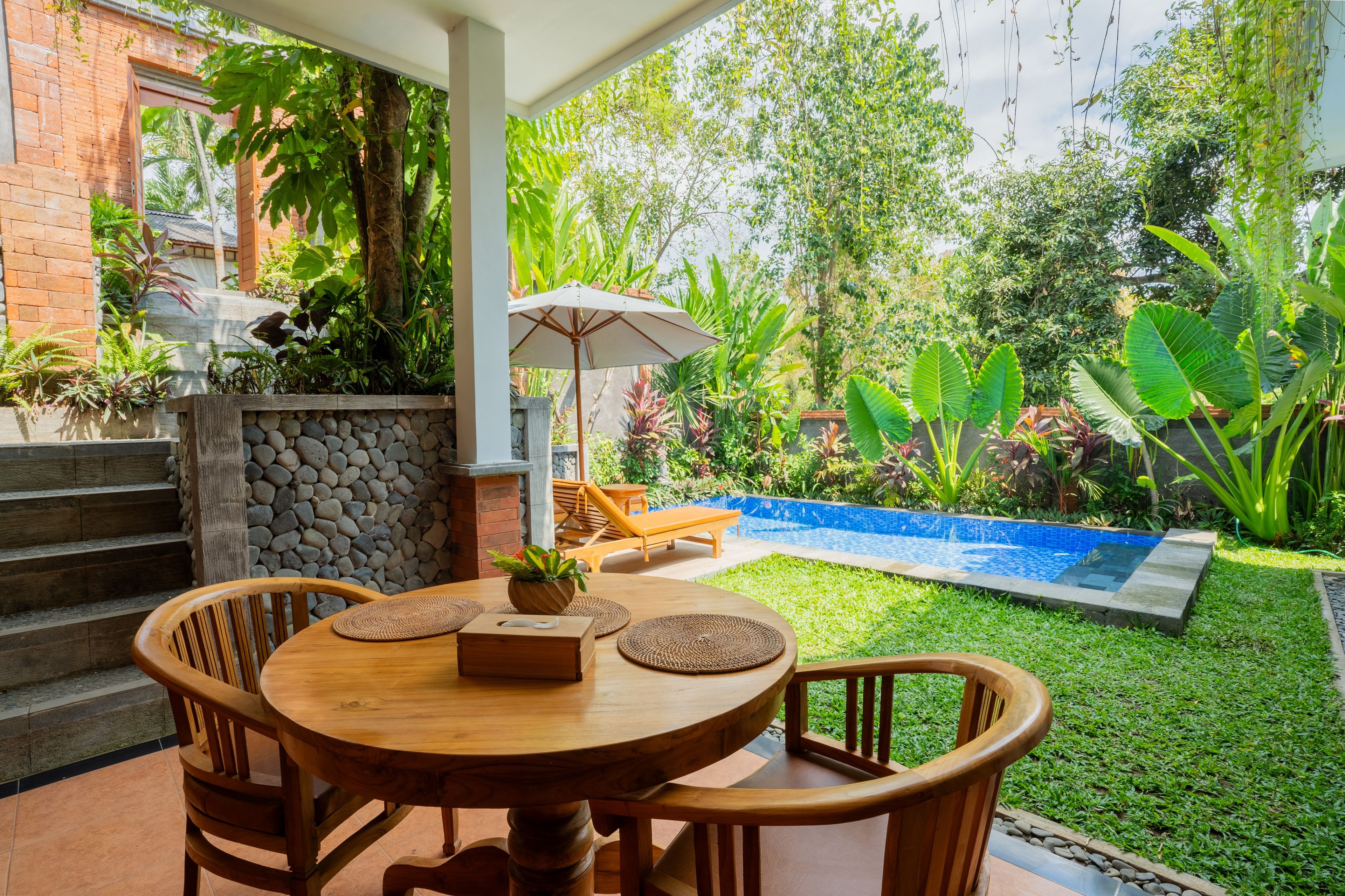 Un patio con una mesa redonda de madera, sillas y una pequeña planta en maceta.