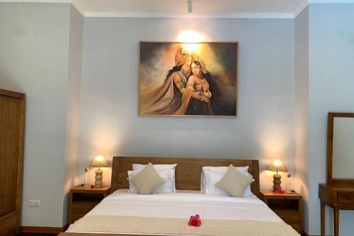 Une chambre d’hôtel avec un lit, deux tables de chevet avec des lampes, un tableau au mur et une tête de lit en bois.