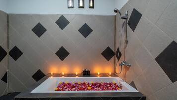 Un baño con una bañera llena de flores, ducha y tres luces empotradas.