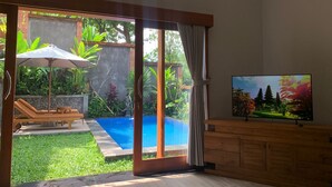 Una habitación con un gran ventanal corredero que da a una zona de piscina, un armario de madera y un televisor en la pared.