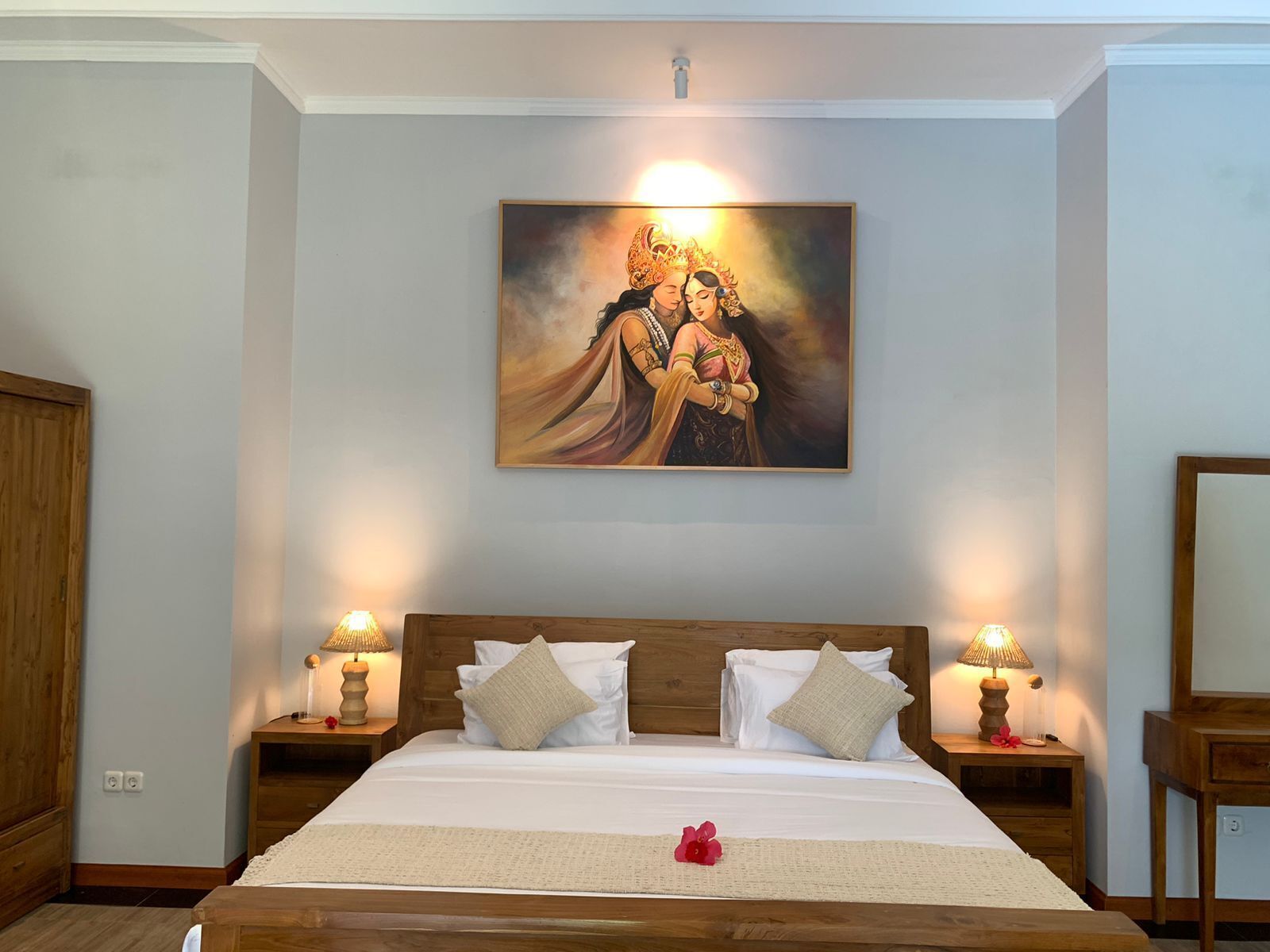 A hotel room with a large bed, two nightstands with lamps, a wooden headboard, and a painting above the bed.
