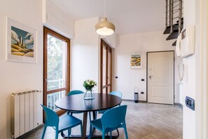 A dining area with a round table, blue chairs, a hanging light fixture, a radiator, and a door with a phone. - GuestHost - Comfortable 91 sqm two- floor modern flat (with internal spiral staircase), 5 min walk from the Colonna San Marco stop, which connects it to the historical centre. With two bedrooms, two bathrooms and a living room, it can accommodate 5 peopl (Siena)