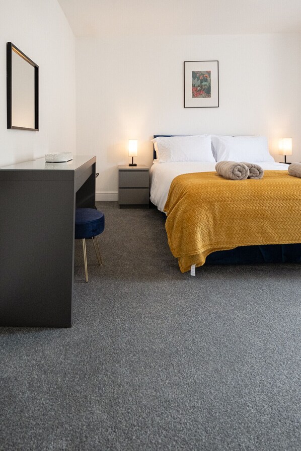 A hotel room with a bed, a desk, and a chair. There are two bedside tables with lamps.