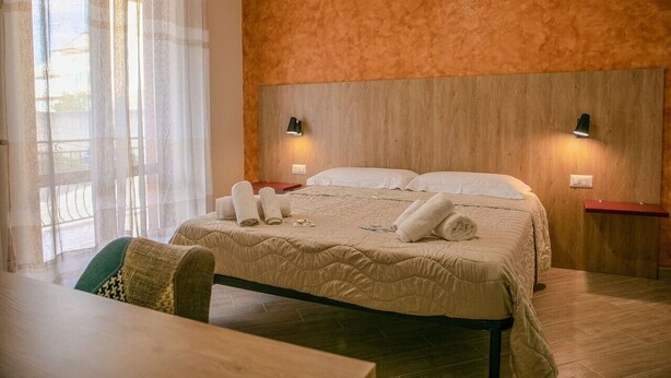 Een hotelkamer met een bed, twee bedlampjes, een houten hoofdeinde, een tafel en een stoel.