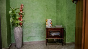 Een hoek met een groen gestructureerde muur, een hoge vaas met rode bloemen en een klein houten bijzettafeltje met een lijstfoto en een boek.