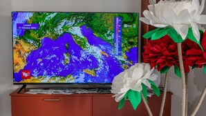 A television displaying a weather forecast map, placed on a wooden cabinet with a handle.