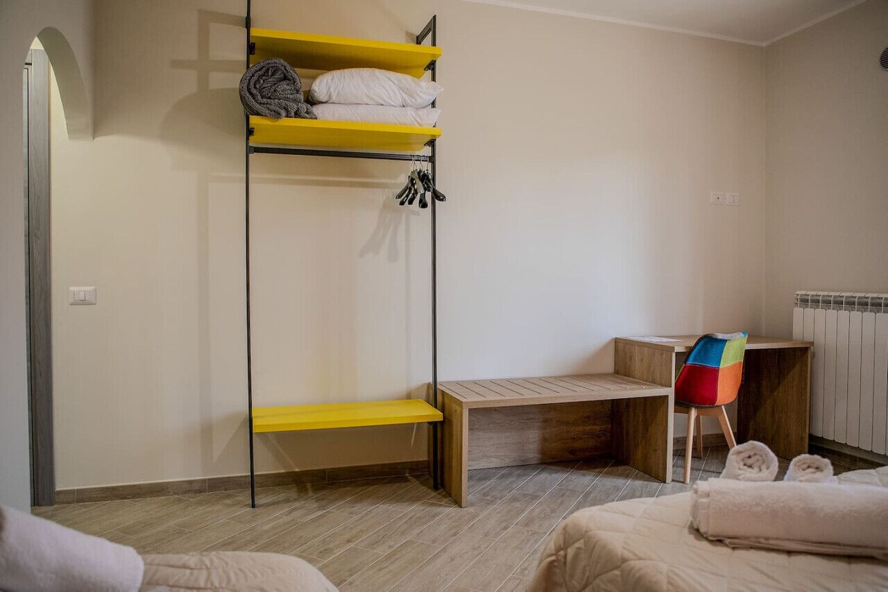 A compact room with a bunk bed, a wooden desk, a colorful chair, and a radiator.