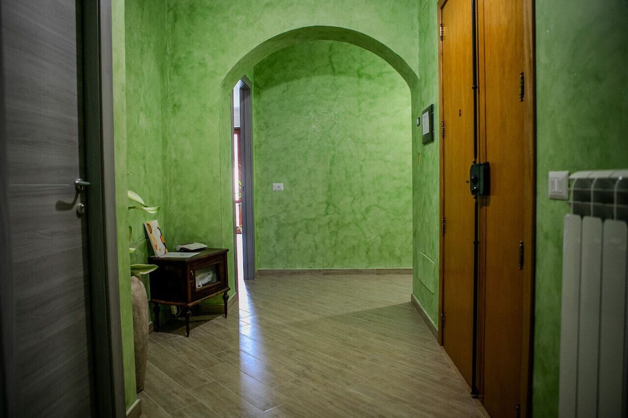 Un couloir aux murs verts, une porte en bois et un radiateur.