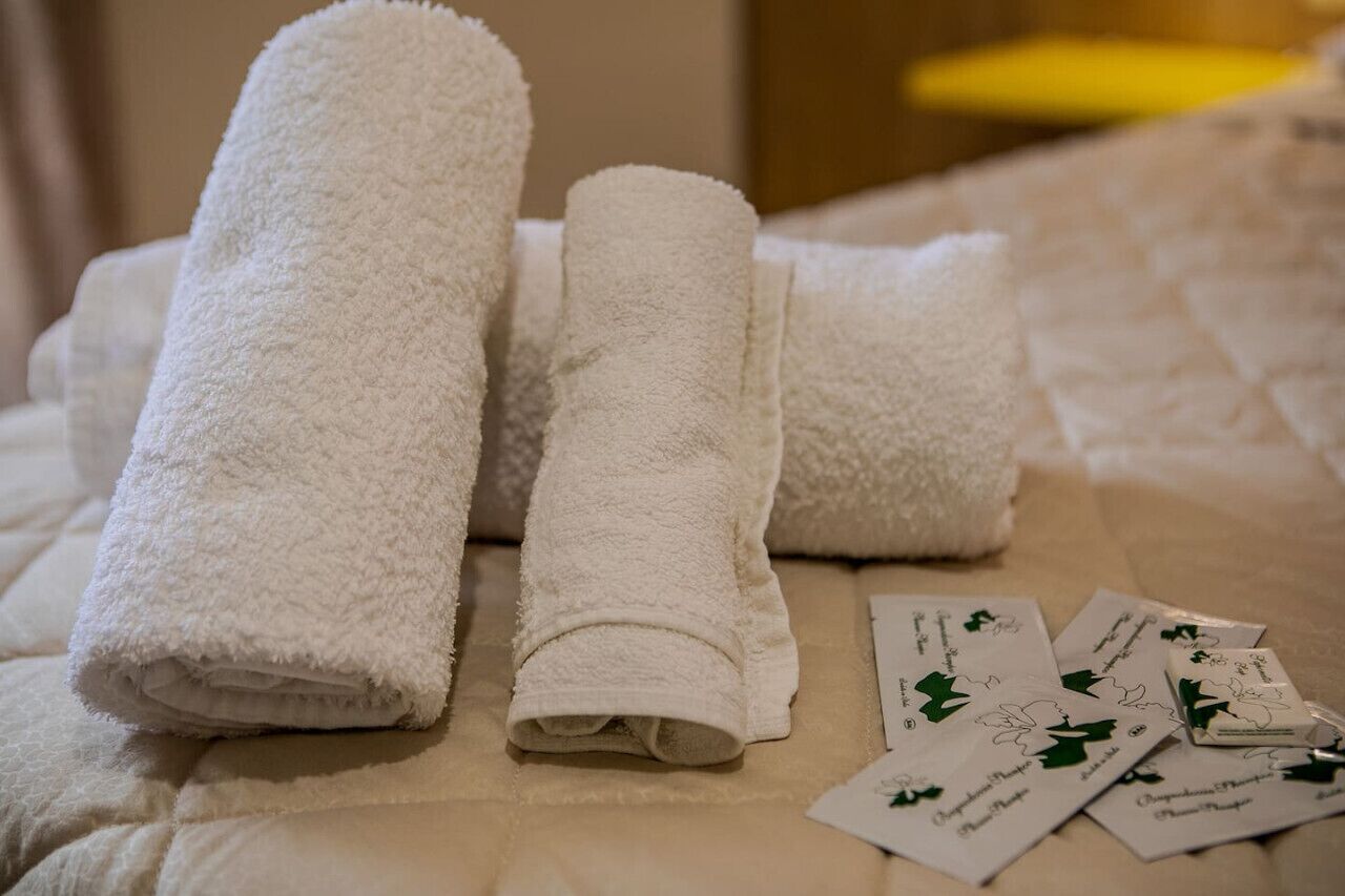 Un lit bien fait, avec trois serviettes blanches pliées et quelques cartes décorées de motifs de feuilles vertes.