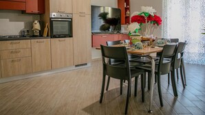 A modern kitchen with wooden cabinets, a built-in oven, and a dining area with a table and chairs.