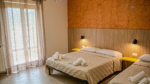 A hotel room with two beds, a wooden headboard, a window with curtains, and bedside lamps.