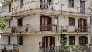 A multi-story building with balconies, windows with shutters, and potted plants.