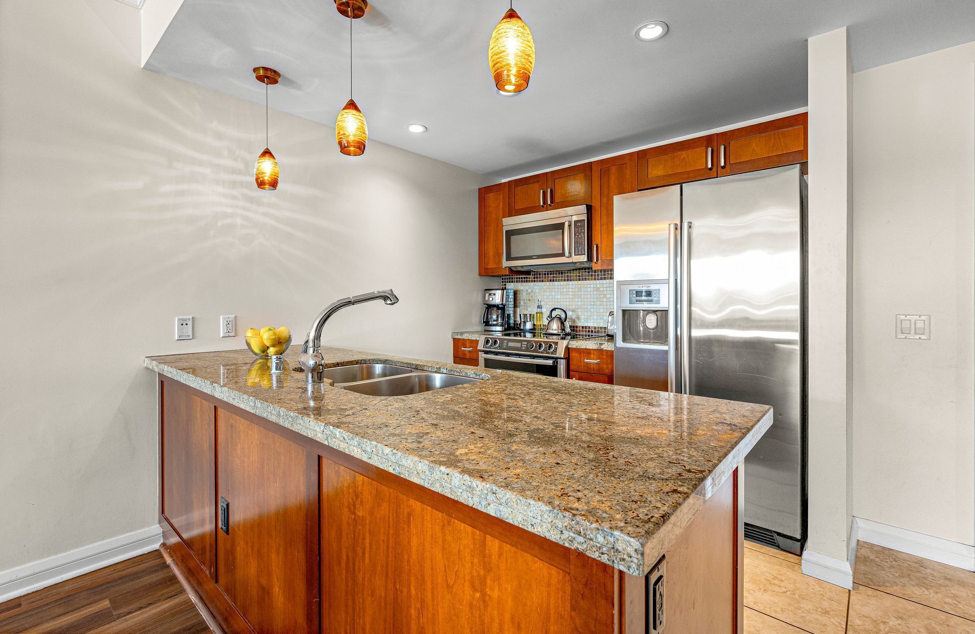 Una cocina con encimeras de granito, armarios de madera, electrodomésticos de acero inoxidable e iluminación colgante.