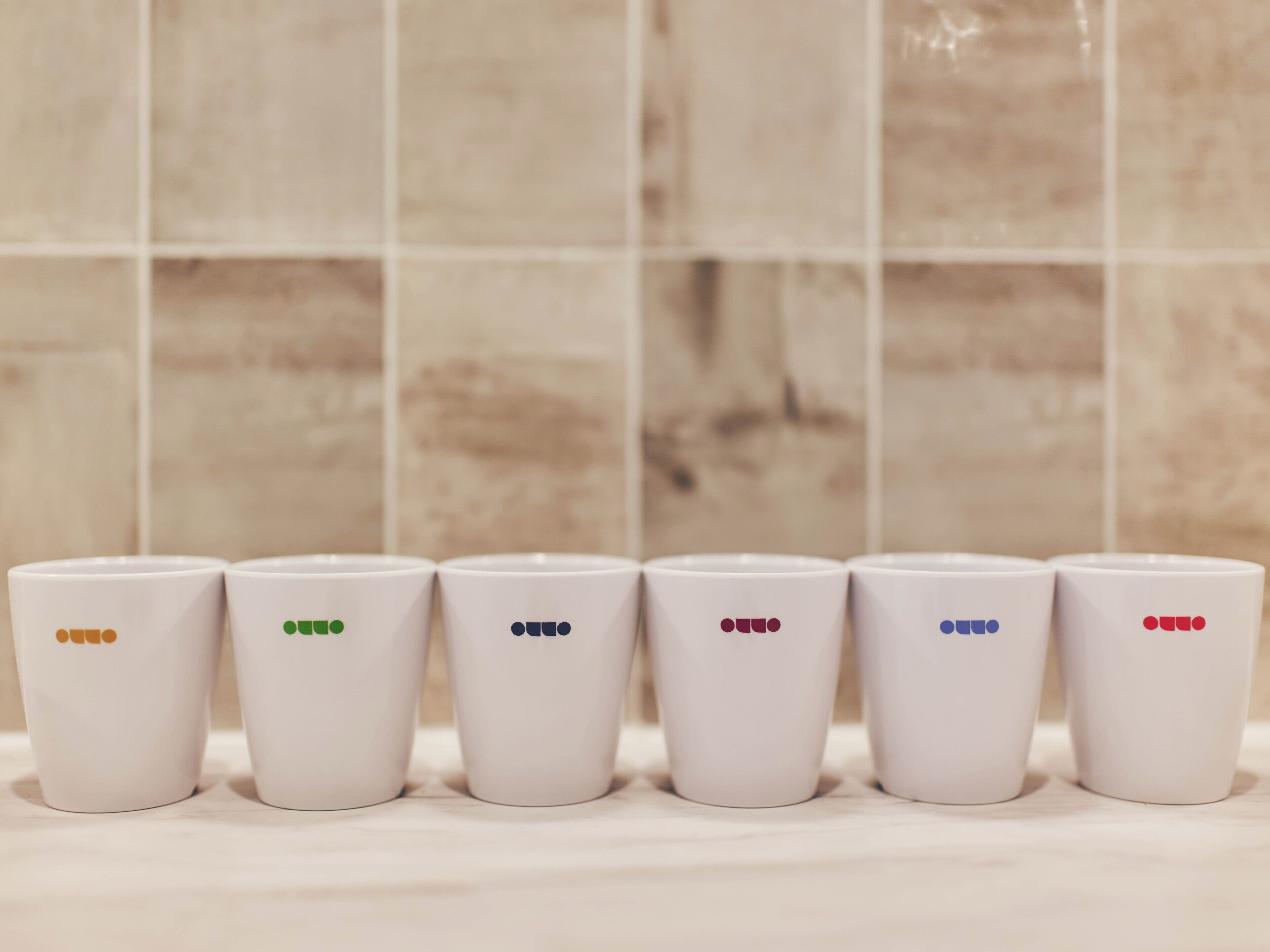 Six white cups with colored dots arranged in a row on a surface.