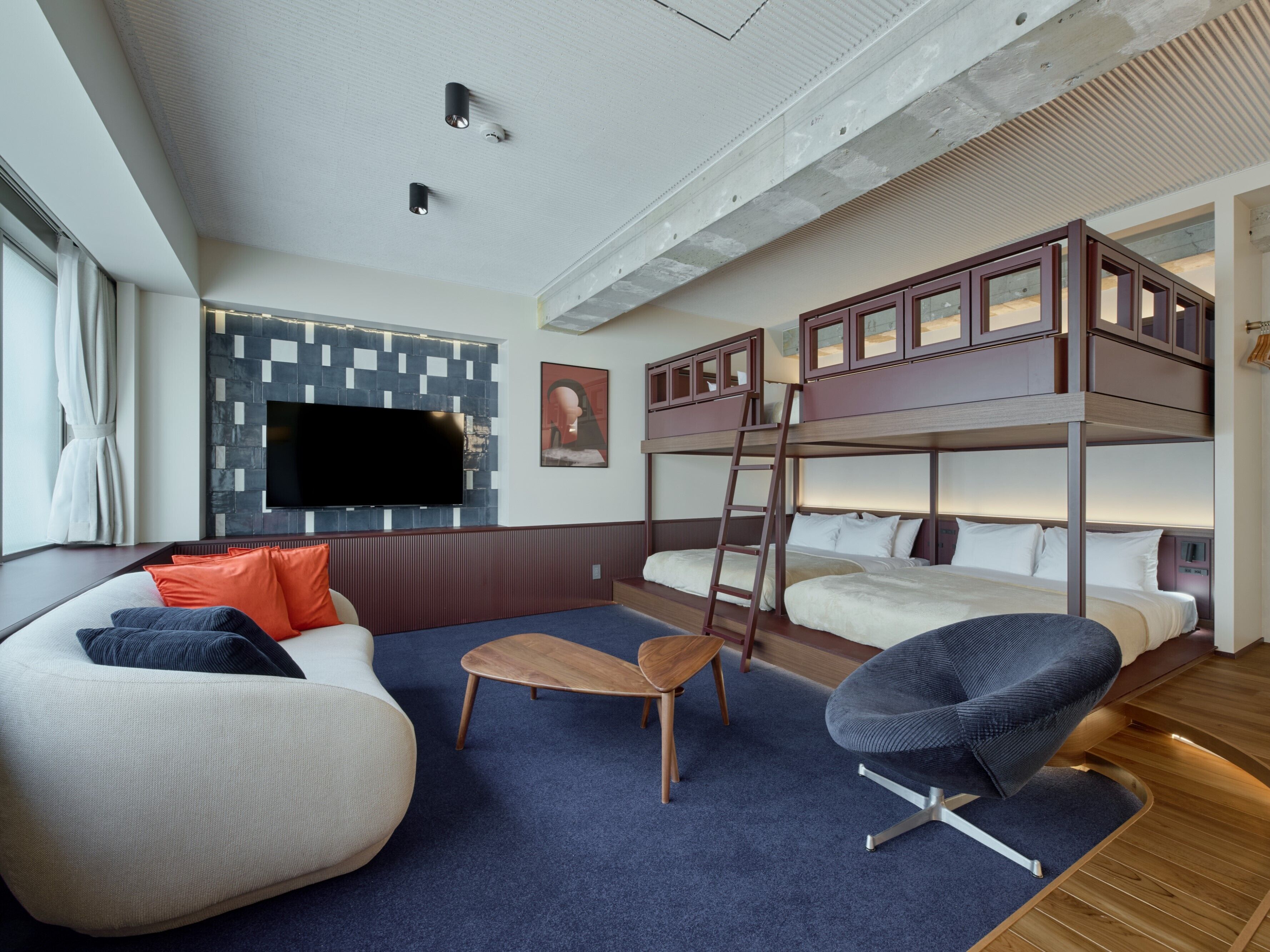 A modern hotel room with bunk beds, a flat-screen TV, a sofa, a chair, and a wooden coffee table.