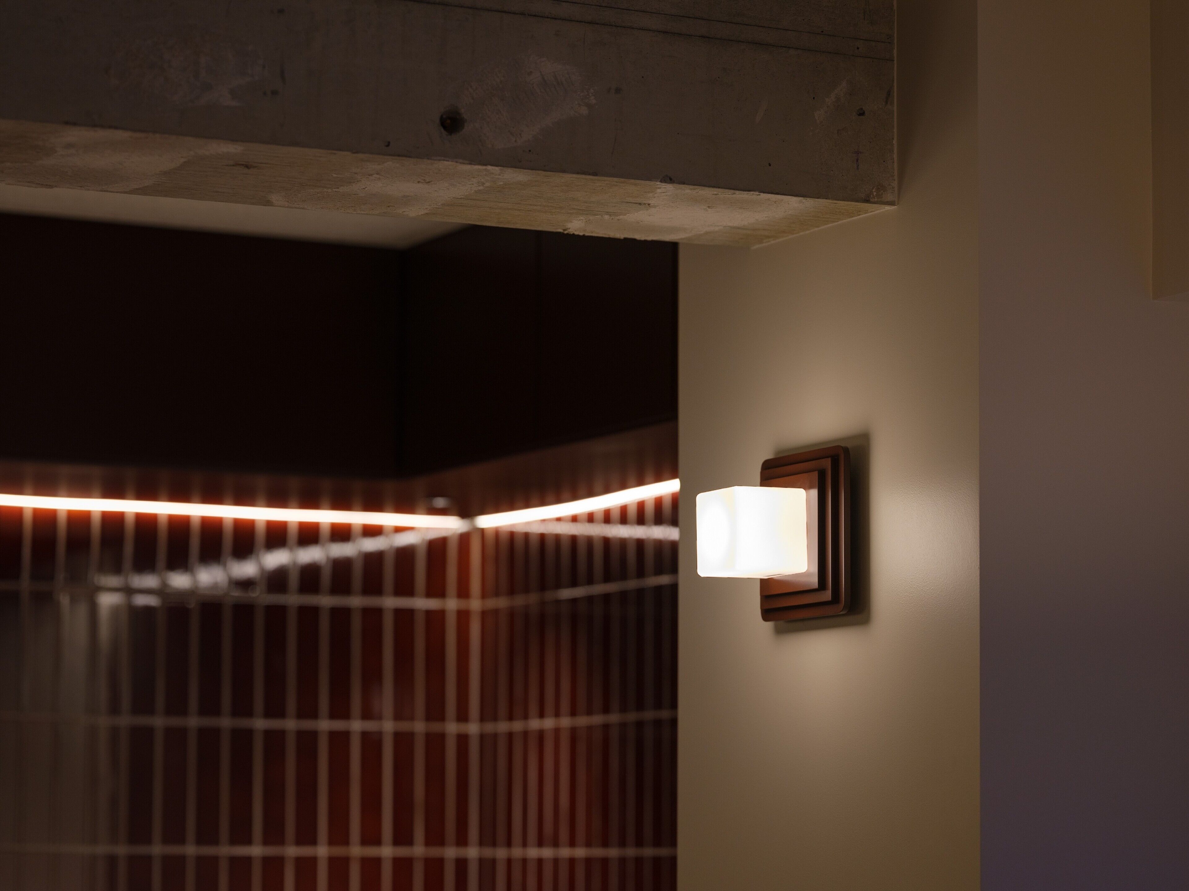 A corner of a room with a light fixture on the wall and a wooden slat design on the ceiling.
