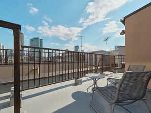 A rooftop terrace with a metal railing, two wicker chairs, a small table, and a view of the city skyline. - illi Tex Aoyama (Tokyo)