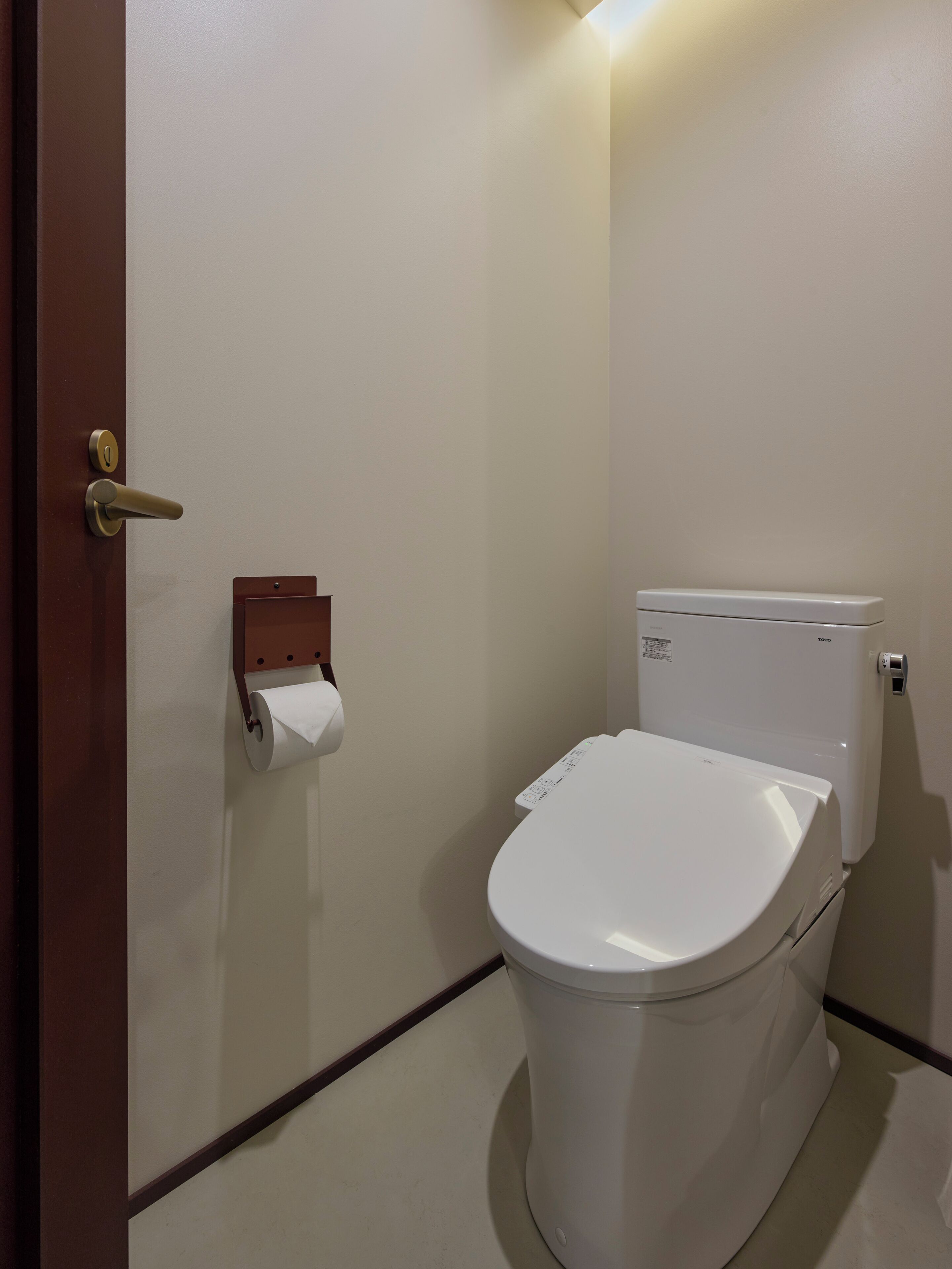 Et hvidt toilet med en TOYO tank, en papirhåndklædedispenser og en dør med et gyldent håndtag.