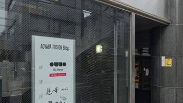 En bygning med et stort glasvindue, der viser skilte for 'AOYAMA FUSION Bldg.' og 'iLLi StayS illi Tex Aoyama'.