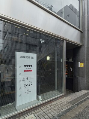 A building with a large glass window displaying a sign for 'AOYAMA FUSION Bldg.' and 'iLLi StayS illi Tex Aoyama.' - illi Tex Aoyama (Tokyo)