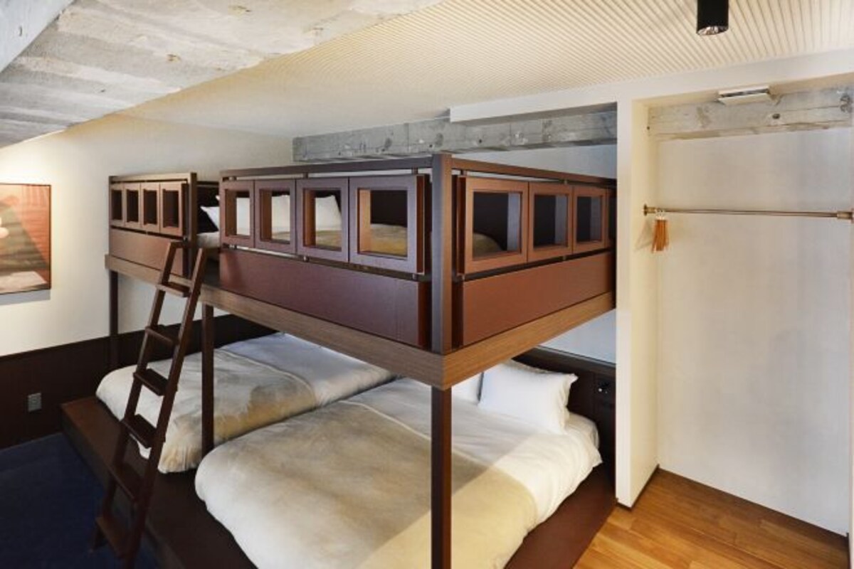 A bunk bed with a ladder, white bedding, and a wooden floor.