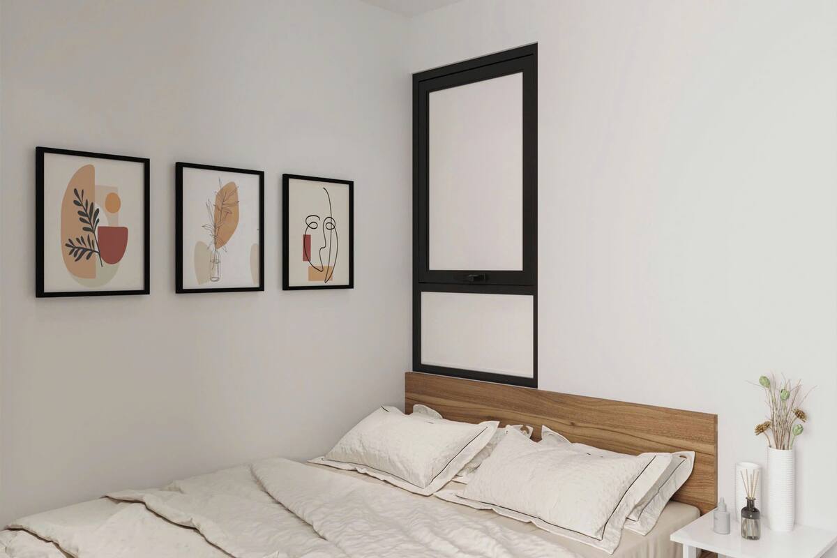 A bedroom with a bed, white bedding, a bedside table with a vase, and three framed artworks on the wall.