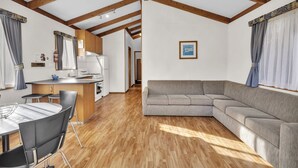 Una cocina moderna con vigas de madera, un comedor con mesa y sillas, y una sala de estar con sofá y cortinas.
