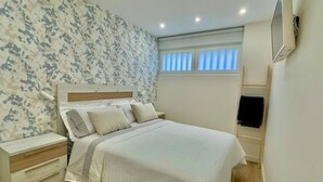 A bedroom with a bed, nightstands, a dresser, a window with blinds, and a wall-mounted air conditioning unit. - Ogoño apartment Bermeo (Bermeo)
