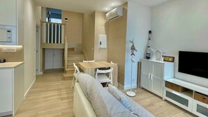 A modern living room with a sofa, a dining table, and a TV. There is a staircase leading to an upper level. - Ogoño apartment Bermeo (Bermeo)