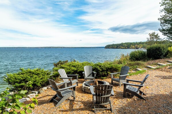 A lakeside seating area with Adirondack chairs and a fire pit.