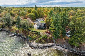 A house surrounded by dense forest with a rocky shoreline and a small dock.
