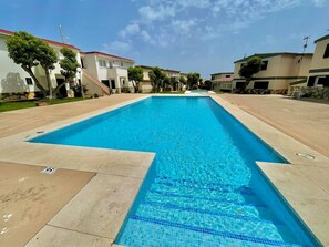 Uma piscina retangular com água azul cristalina, ladeada por um calçadão pavimentado.
